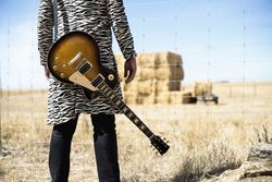 Person with guitar behind back in front of barbed wire