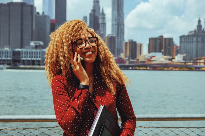 Happy Black female speaking on smart phone by Hudson River
