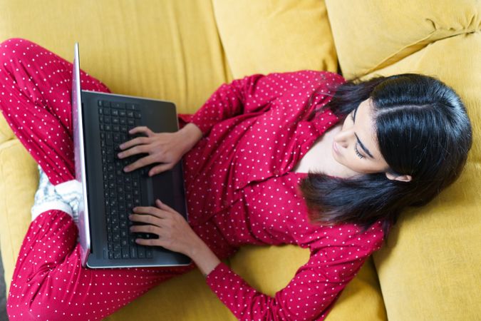 Female relaxing at home using computer on yellow sofa