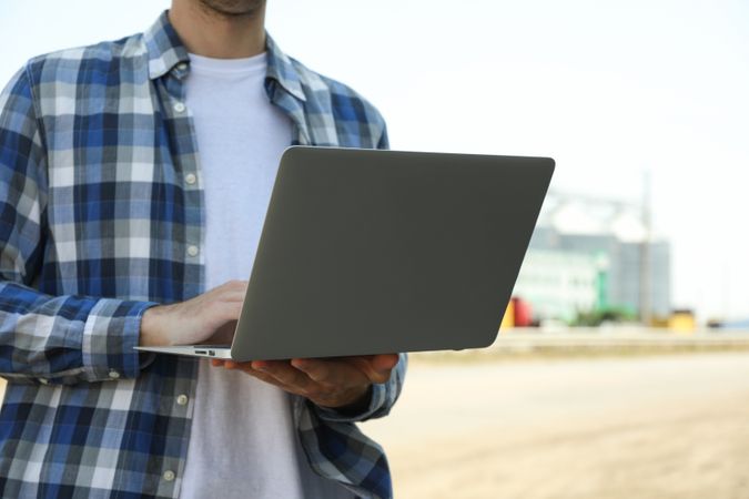 Young man with laptop against grain silos. Agriculture business