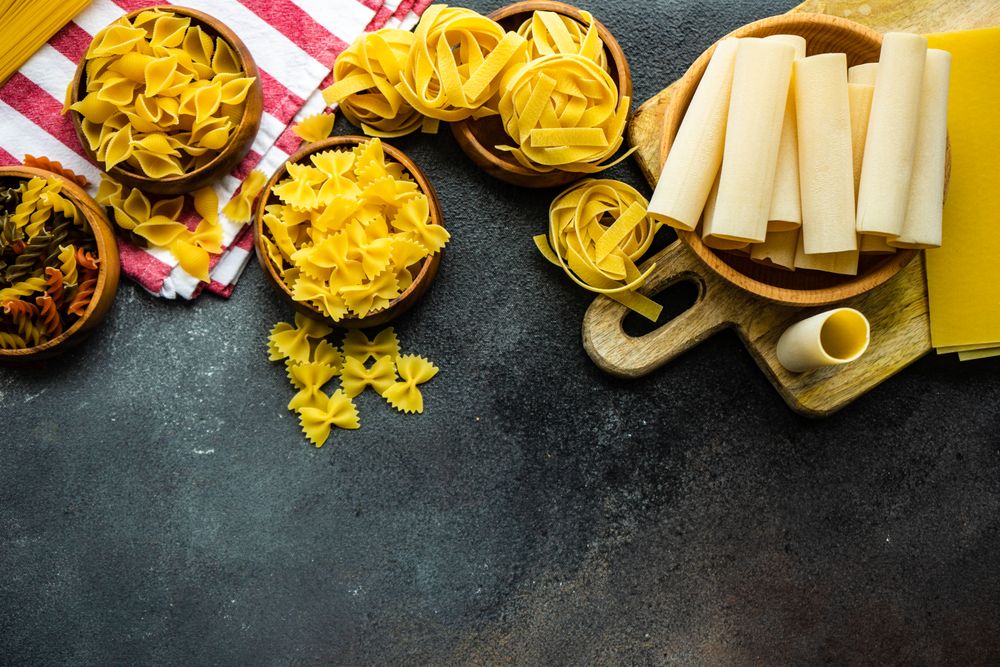Top view of variety of bowls of dry Italian pasta with space for text
