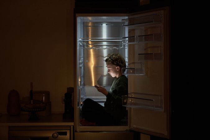 Kid with tablet sitting in fridge