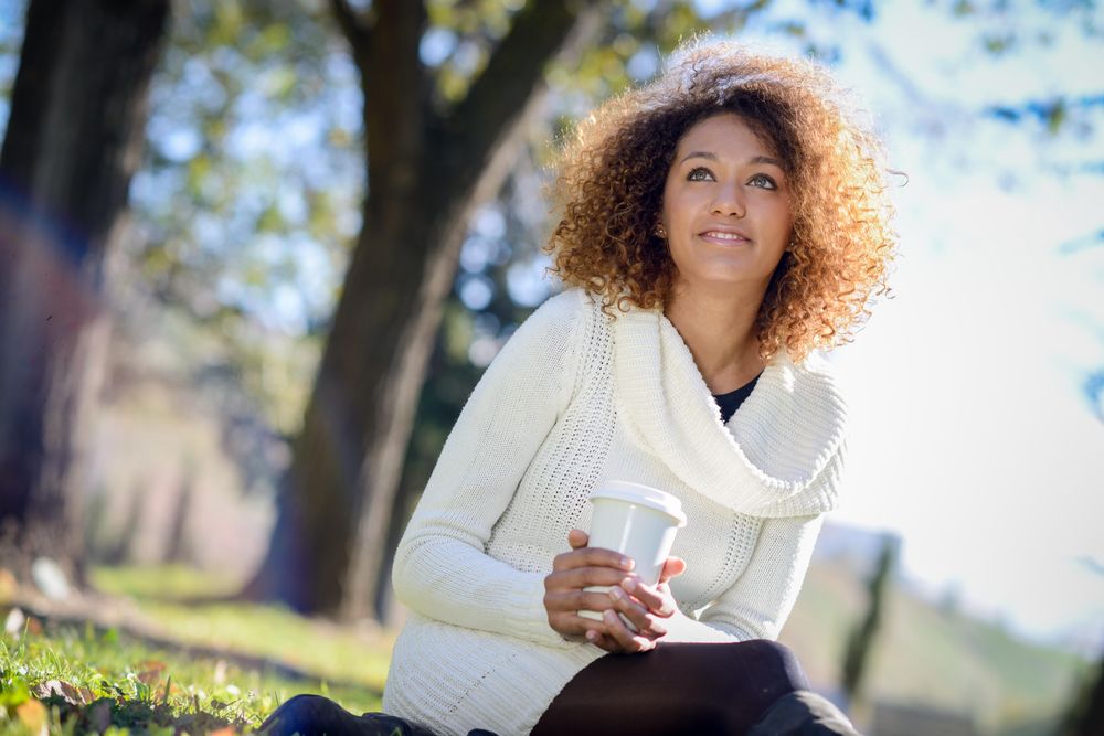 Wistful woman looking in the distance while holding warm drink sitting in park