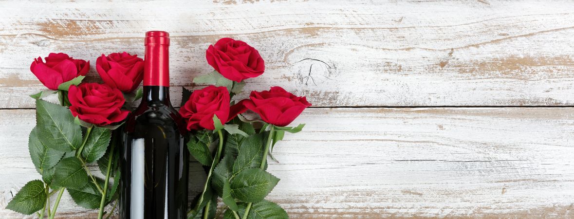 Valentine’s Day celebration with red wine and roses on rustic wooden background