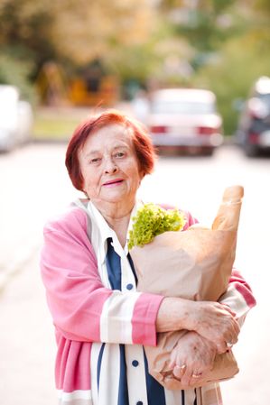 Older woman in pink cardigan holding grocery bag standing outdoor