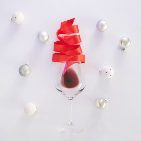 Red Christmas tree ribbon coming out of wine glass surrounded by baubles