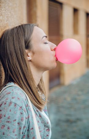 Side view of woman blowing pink bubble with gum