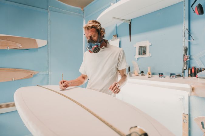 Man in respirator measuring surf board in workshop
