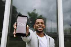 Smiling Black man showing mobile phone with inscription