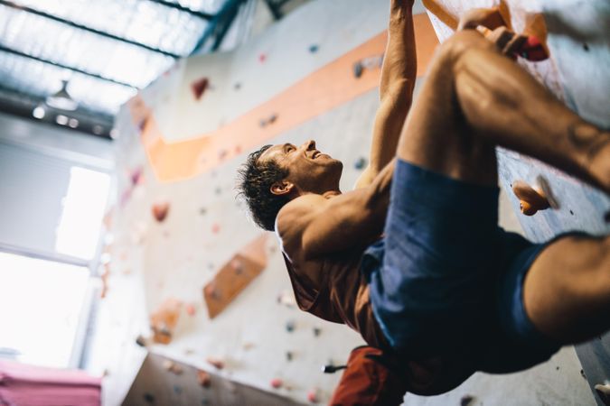Enthusiastic climber practicing rock climbing at rock climbing gym