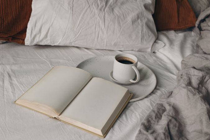 Cup of coffee, open books on bed sheet
