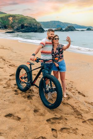 Male and female taking picture with phone standing with bicycle, vertical