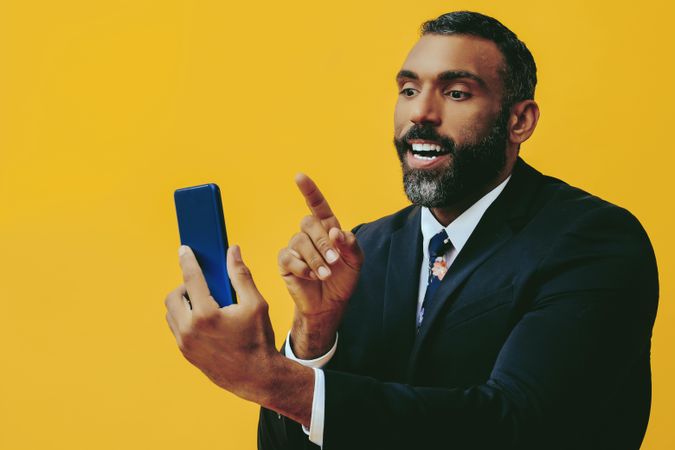Opinionated Black businessman in suit speaking at smartphone screen while pointing