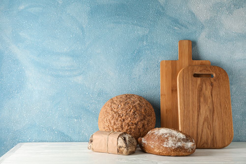 Bakery products and cutting boards on wooden table against light background, space for text