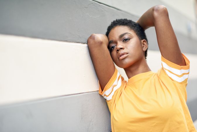 Black woman leaning on grey striped wall with arms up looking in the distance