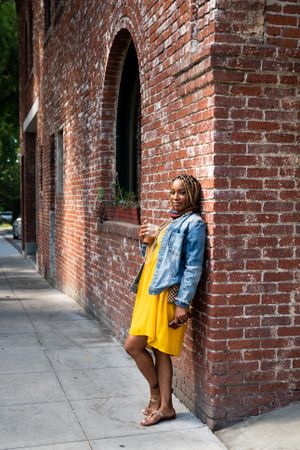 Full length shot of woman leaning against old brick building holding iced coffee looking at camera