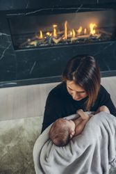 Mother hugging her baby in front of fireplace