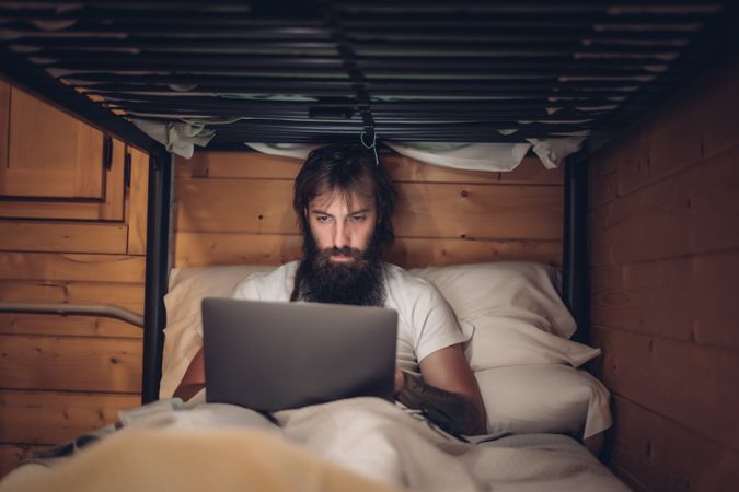 Man using laptop in rustic bunk bed