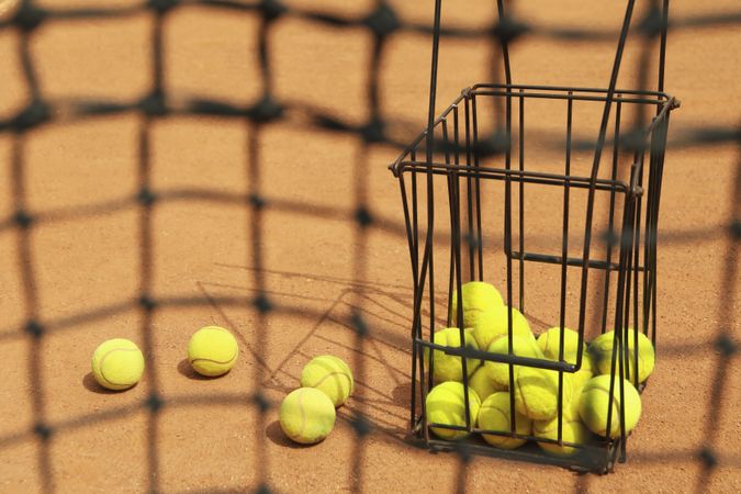 Tennis net against clay court with basket with balls