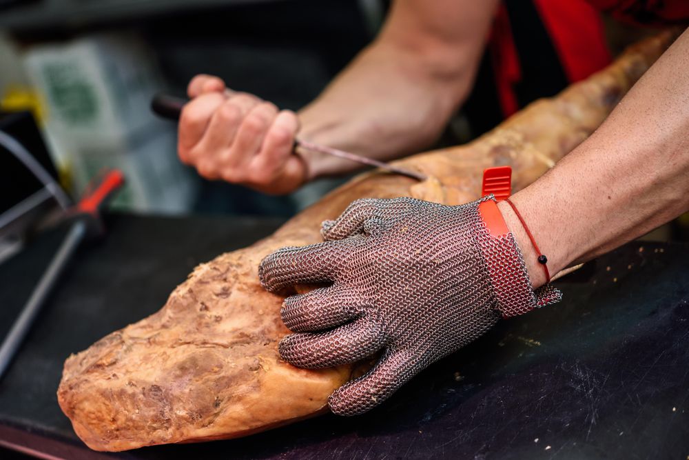 Close up of butcher’s hands holding ham and cutting with knife