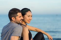 Happy couple in sportswear sitting on beach