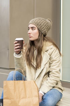 Woman sitting outdoors holding a take away coffee after shopping