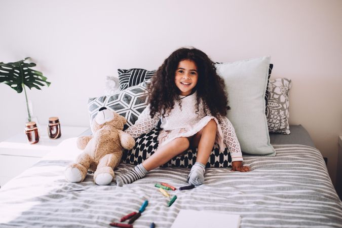 Little girl sitting on the bed smiling with teddy bear