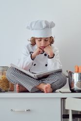 Attentive preteen boy in chef costume reading culinary book