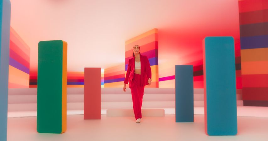 Low Angle Portrait of a Fashionable Young Woman Performing a Catwalk in a Colorful Neon Studio. Stylish Female Walking Confidently In A Bright Lit Room With Geometric Decoration On Set