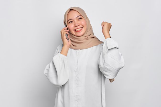 Asian Muslim woman celebrating good news being received through her cell phone