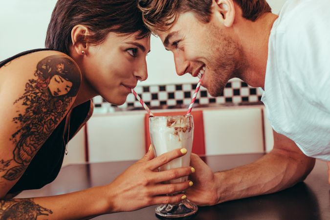 Man and woman sharing milk shake using two straws