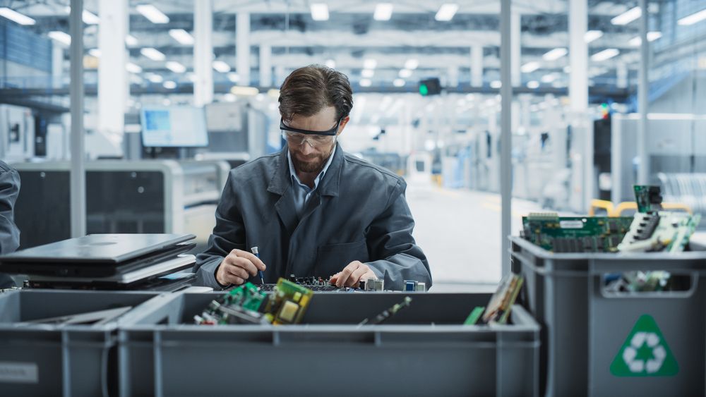 Male Worker Disassembling Old Laptops To Recycle Electronic Components For Sustainable Microchip Production At an Electronics Factory.