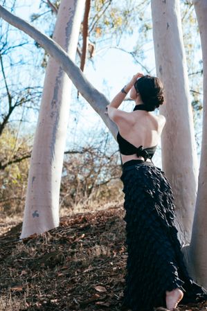 Back view of woman standing near tree in skirt and open backed shirt