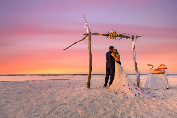 Rear view of couple being married on a beach at sunset