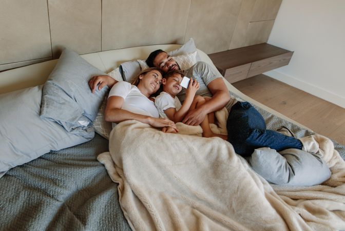 Young family in bedroom looking at cell phone