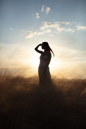 Young woman standing in an open field with hands shielding her eyes