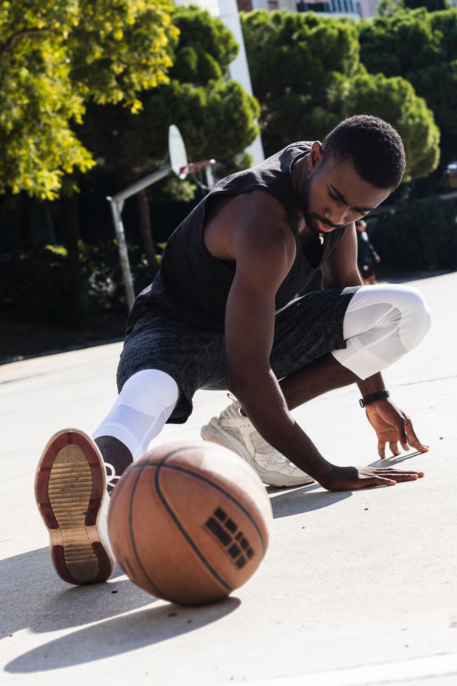Black sportsman stretching on basketball court