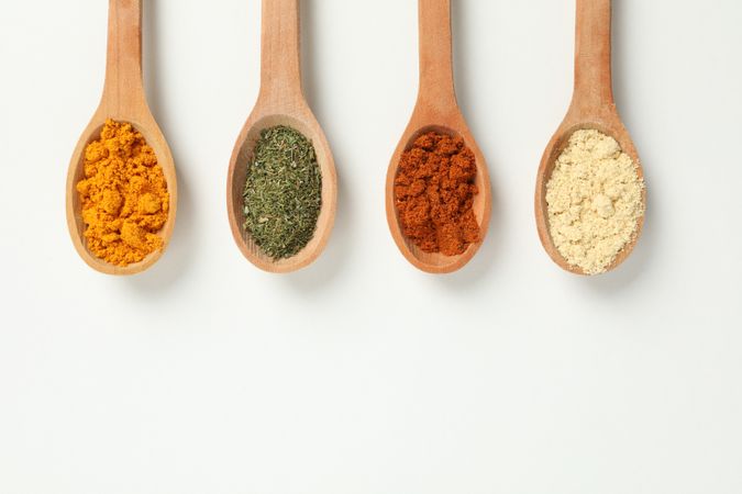 Top view of four wooden spoons full of colorful earth tone spices