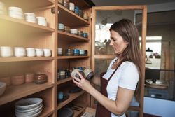 Woman in leather apron holding handmade cups in her shop
