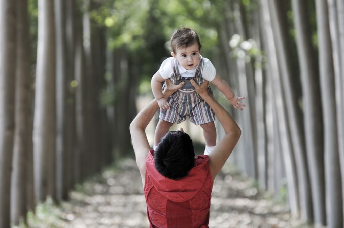 Back of woman holding baby above her head in forest
