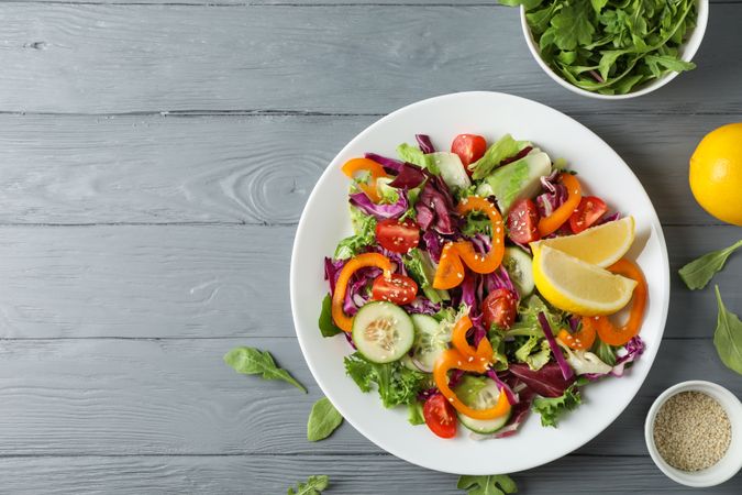 Plate with salad and ingredients on wooden background, top view