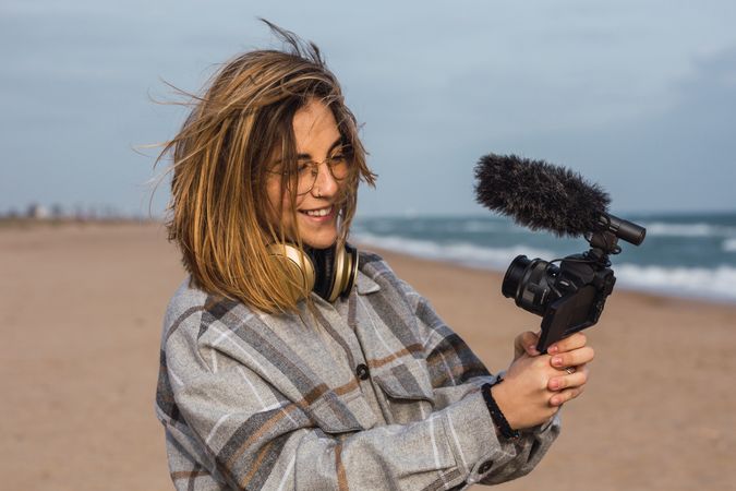 Young woman on seashore and shooting video on camera