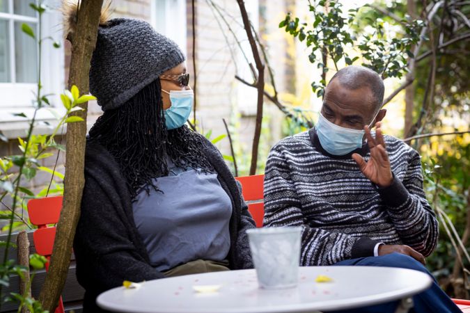 Older Black man and woman sitting outside talking in facemasks