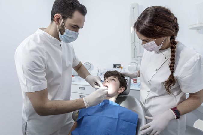 Dentist using tools to check teenage patient's teeth at dental clinic