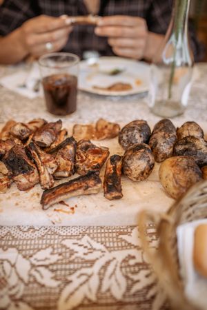 unrecognizable person eating ribs and potatoes from barbeque in the table