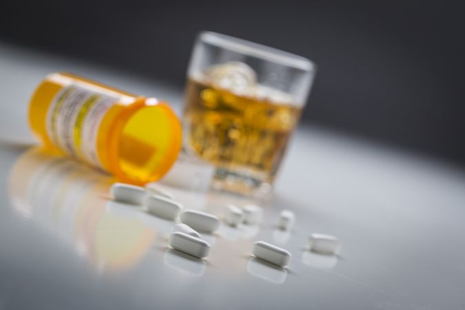 Prescription Drugs Spilled From Fallen Bottle Near Glass of Alcohol