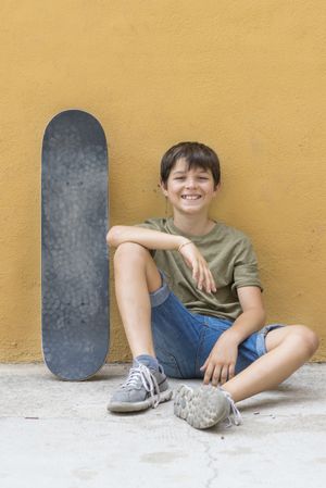 A smiling boy with skateboard sitting alone