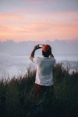 Back view of man taking photo of sunset horizon with smartphone