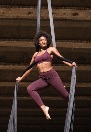 Slim woman doing yoga with aerial silks in city