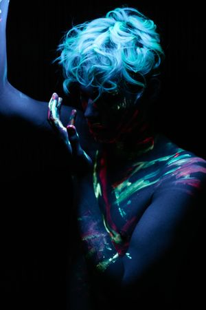 Topless young man with UV body paint in a dark room